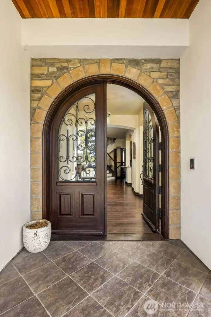 Front Entry: Dramatic arched wood door framed by stone tile and warm architectural detailing.