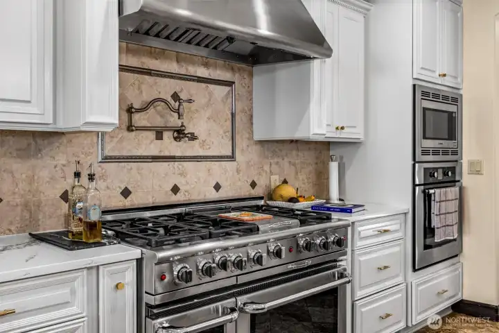 Main Floor Kitchen: Detailed view of the professional range, custom hood, and elegant tile backsplash.