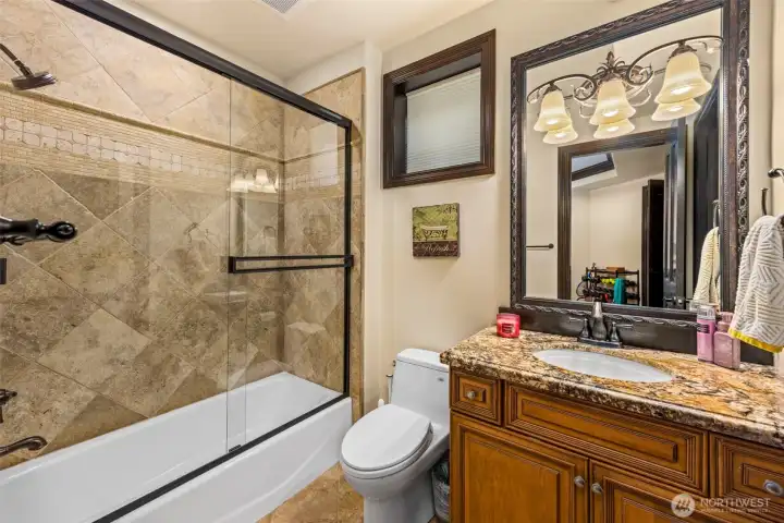 Lower level bathroom: Lower-level bath featuring tiled shower, granite vanity, and warm wood cabinetry.