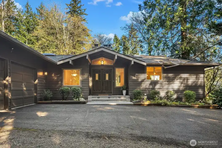 This beautiful wide-angle view showcases the home's expansive single-story profile, circular pull-through driveway with ample parking, and stunning natural setting surrounded by mature Pacific Northwest evergreens. The thoughtfully designed exterior seamlessly blends into the lush, private landscape while offering plenty of space for a boat or RV.