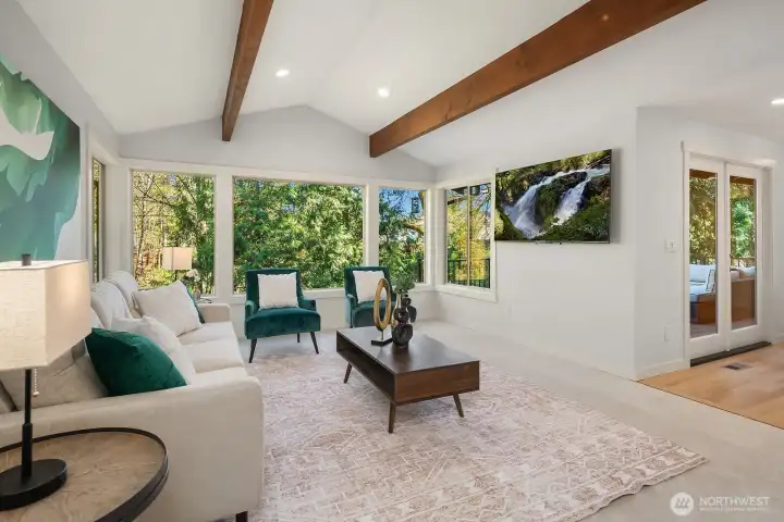 This alternate view of the living room further highlights the seamless flow of the open-concept main level, with gorgeous beamed ceilings, fresh interior paint, and an abundance of natural light pouring through the large windows overlooking the private, tree-lined backyard. The refined yet comfortable space is perfect for gathering with family and friends.