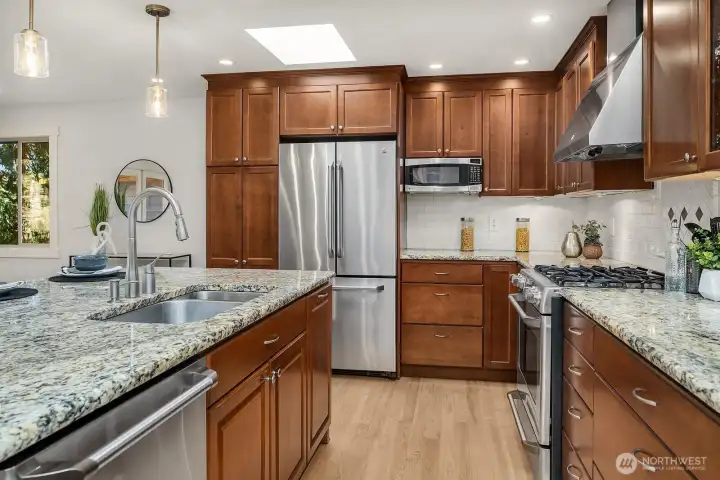 A closer look at the kitchen reveals beautiful granite countertops, rich wood cabinetry with ample storage, and premium stainless steel appliances including a double oven and French door refrigerator. Updated lighting and refinished hardwood floors complete this thoughtfully designed space that perfectly balances form and function.