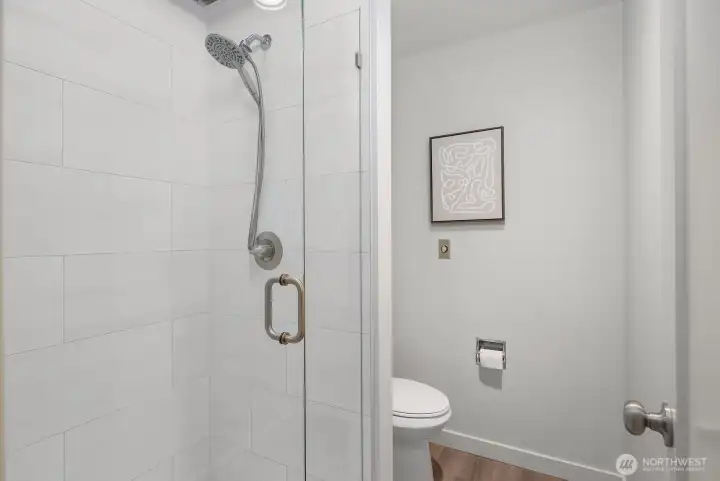 This smartly updated bathroom features a sleek, floor-to-ceiling tiled walk-in shower with a modern rainfall-style fixture, offering a clean and contemporary spa-like experience. The crisp white finishes and quality fixtures reflect the thoughtful updates found throughout this exceptional home.