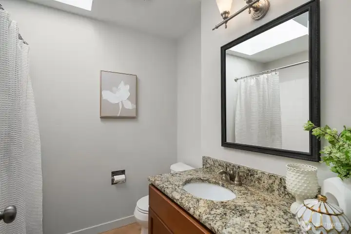 The lower level's updated 3/4 bath features a stylish granite-topped vanity, bold framed mirror, and clean, contemporary finishes that perfectly complement the ADU's thoughtful design. This well-appointed bath provides comfort and privacy for lower level guests or extended family members.