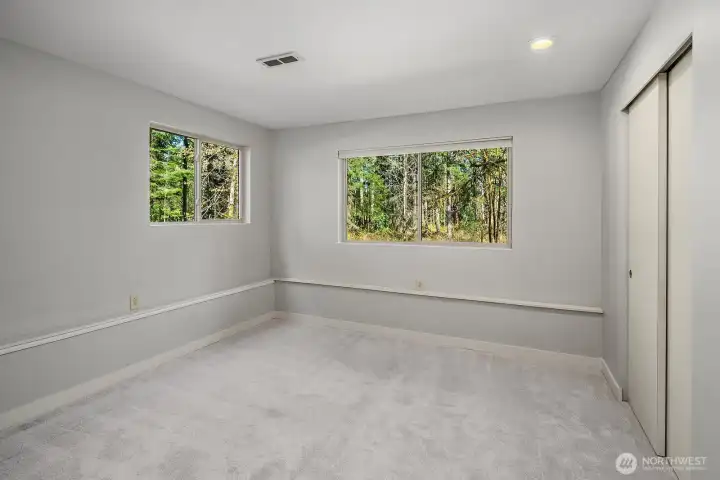This alternate view of the lower level bedroom highlights the generous room size, dual windows that bring in ample natural light and treetop views, and the fresh new carpet and paint that carry the home's quality updates throughout every level. A comfortable and private space that adds exceptional value to the home's flexible ADU configuration.