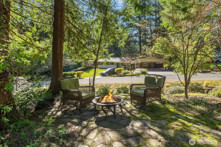 This enchanting backyard fire pit area provides the perfect outdoor gathering spot, nestled among mature evergreens and lush landscaping for a wonderfully private and serene setting. Whether roasting marshmallows with family or enjoying an evening under the stars with friends, this magical outdoor space captures the very best of Pacific Northwest living.