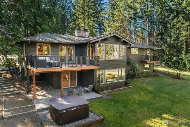 This inviting rear exterior view highlights the home's exceptional outdoor living setup, featuring the upper main level deck, the lower level covered patio, and the relaxing hot tub perfectly positioned to enjoy the lush, private backyard surroundings. This incredible multi-level outdoor living space truly embodies the best of Pacific Northwest indoor-outdoor lifestyle living.