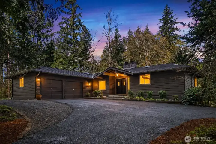 This breathtaking twilight shot captures the home's warm and welcoming glow as interior lights illuminate the expansive single-story profile against a stunning dusk sky, showcasing the circular pull-through driveway and lush mature landscaping at their most magical. A truly captivating image that perfectly conveys the beauty, privacy, and charm of this exceptional Sammamish retreat.