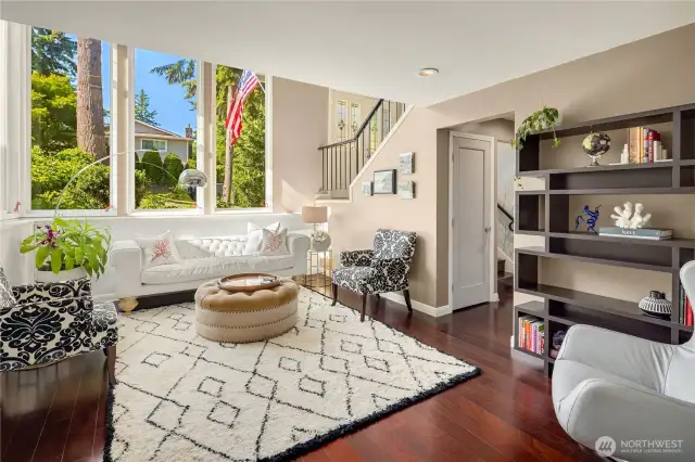Bathed in natural light, this stunning living room features soaring double-height ceilings and expansive picture windows framing lush greenery. Elegant design details include a tufted sofa, statement lighting, and a graceful staircase—creating a warm, welcoming first impression....