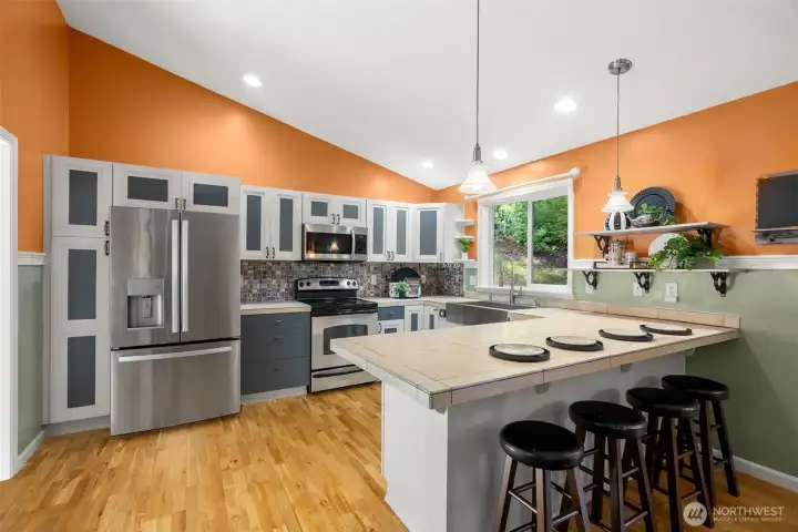 Kitchen with barstool seating, stainless steel appliances, oversized tile counntertops