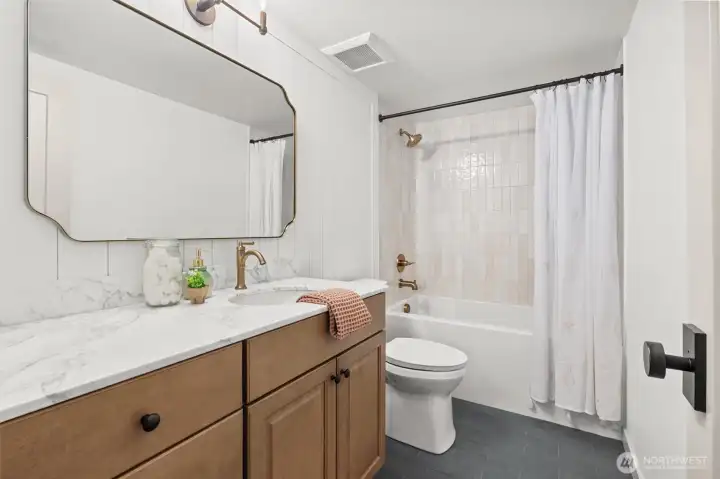 Lower-level full guest bathroom with deep soaking tub, custom tile surround, slate tile flooring, vanity with soft close drawers/doors, marble countertop, shiplap wall detail and high-end plumbing fixtures.