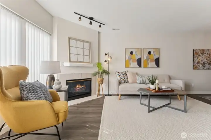 Anchoring the living area is a cozy gas fireplace with a tile surround—perfect for relaxing evenings at home. Large windows invite natural light and provide peaceful views toward the backyard and surrounding greenery.