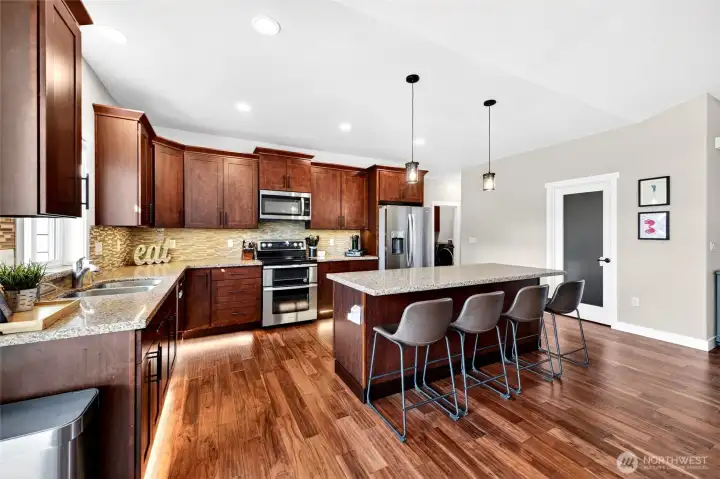 Chef-inspired kitchen featuring granite countertops, oversized island with seating, stainless steel appliances, and abundant cabinetry.