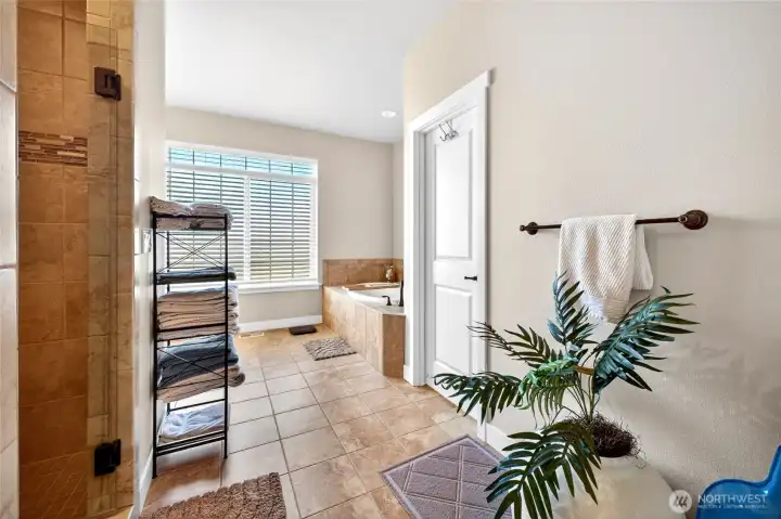 Luxurious primary bath featuring tile flooring, oversized walk-in shower, soaking tub, and abundant natural light.