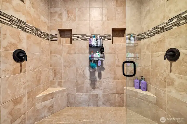 Spa-inspired walk-in tile shower with dual shower heads, built-in benches, and decorative accent tile.