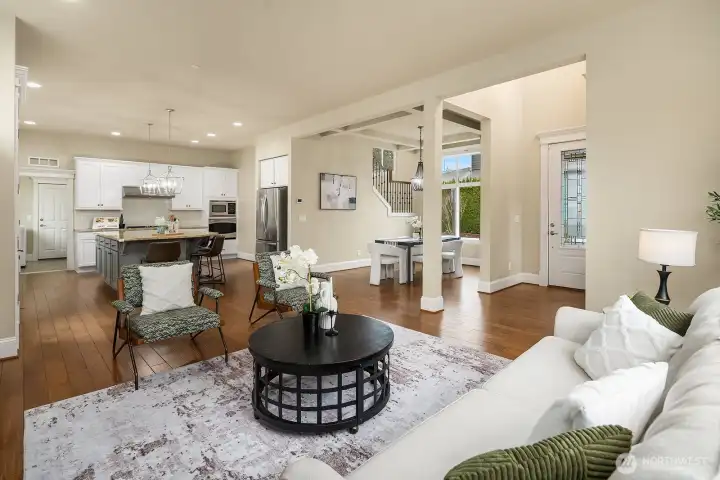 This view showcases the seamless flow between the living room and the expansive kitchen beyond, highlighting the home's open and connected layout with rich engineered hardwood floors anchoring the entire main level. This view showcases the seamless flow between the living room and the expansive kitchen beyond, highlighting the home's open and connected layout with rich engineered hardwood floors anchoring the entire main level.