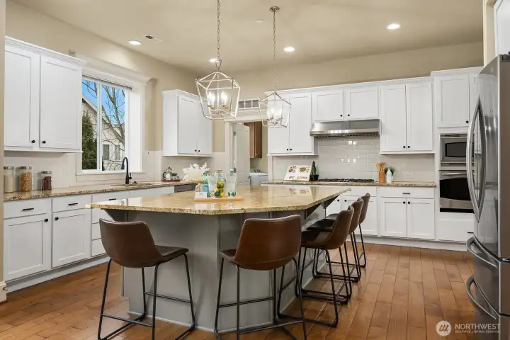 Another angle of the kitchen showcases the generous wraparound island, elegant pendant lighting, and premium appliances — a beautifully designed space that flows effortlessly for both everyday cooking and entertaining. Another angle of the kitchen showcases the generous wraparound island, elegant pendant lighting, and premium appliances — a beautifully designed space that flows effortlessly for both everyday cooking and entertaining.