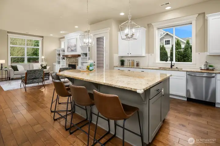 This sweeping view of the kitchen and living areas captures the home's seamless open-concept flow, with the large island, warm hardwood floors, and abundant natural light creating an inviting and cohesive space perfect for gathering. This sweeping view of the kitchen and living areas captures the home's seamless open-concept flow, with the large island, warm hardwood floors, and abundant natural light creating an inviting and cohesive space perfect for gathering.