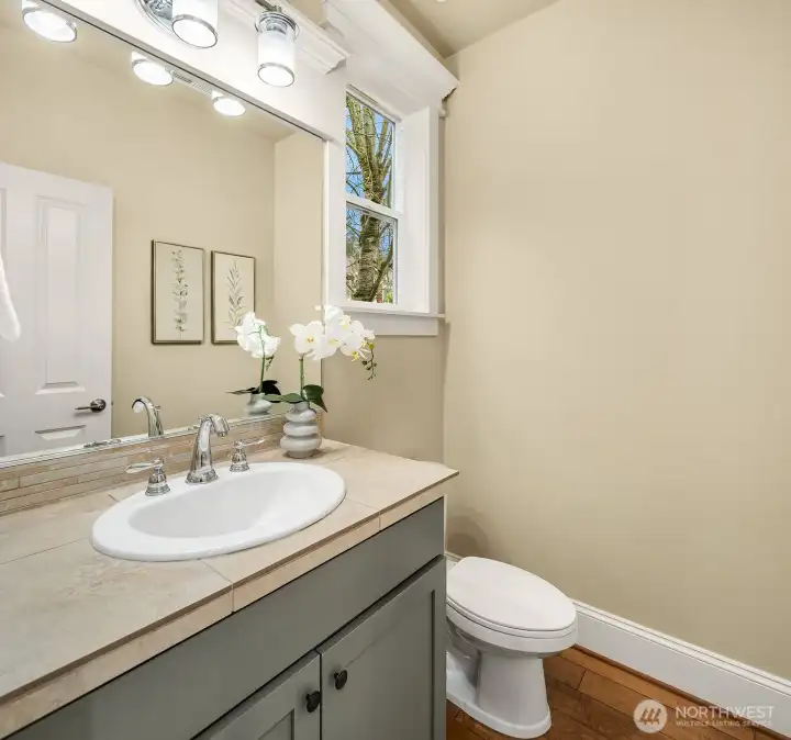 A stylish powder room on the main level features a warm vanity with classic finishes and a large mirror — a polished and practical space for guests and everyday use. A stylish powder room on the main level features a warm vanity with classic finishes and a large mirror — a polished and practical space for guests and everyday use.