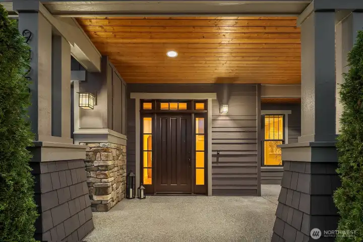 Covered front entry with rich wood front door, cedar soffits, stone accents, and elegant Craftsman details creates a warm first impression for this luxury Kirkland home.
