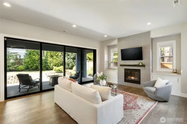 This bright and inviting living room offers seamless indoor-outdoor flow with full-length sliding glass doors that open to a private patio retreat. A sleek gas fireplace, lovely built-ins, and wide-plank wood floors create a cozy yet modern space for gathering or relaxing.