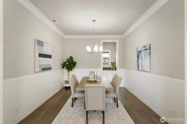 This elegant formal dining room features crisp wainscoting, warm hardwood floors, and a modern light fixture, creating a refined space for entertaining. A convenient pass-through leads to the drop zone, adding both function and flow to this thoughtfully designed layout.