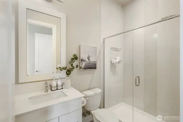 This en suite bath attached to the main-level guest bedroom offers sleek, modern finishes with a glass-enclosed shower, stylish tile detail, and a quartz-topped vanity. Thoughtfully designed for both comfort and elegance, it provides a private and polished space for guests