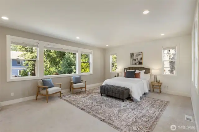 The serene primary suite is bathed in natural light, with expansive windows framing views of lush greenery. Spacious and elegant, it features a cozy sitting area and soft neutral tones, creating a peaceful retreat to unwind and recharge.