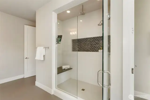 This alternate view of the primary bath highlights the spacious walk-in shower, complete with a built-in bench, dual showerheads—including a rain option—and stylish mosaic tile accent. It’s a luxurious, spa-like escape designed with both comfort and elegance in mind.