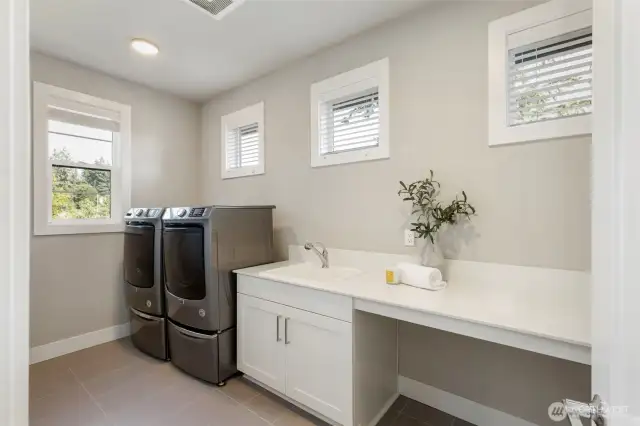 This upstairs laundry room is bright, spacious, and thoughtfully designed with a deep utility sink, extended folding counter, and built-in cabinetry for storage. Please note: the washer and dryer are not included in the sale.