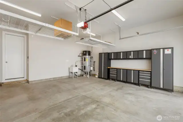 This spacious two-car garage is fully equipped with overhead storage racks, a utility sink, and a custom wall-mounted cabinet system with workbench—perfect for hobbies, tools, and organized storage. It also features an electric car charger, making it ideal for modern living and eco-conscious convenience.