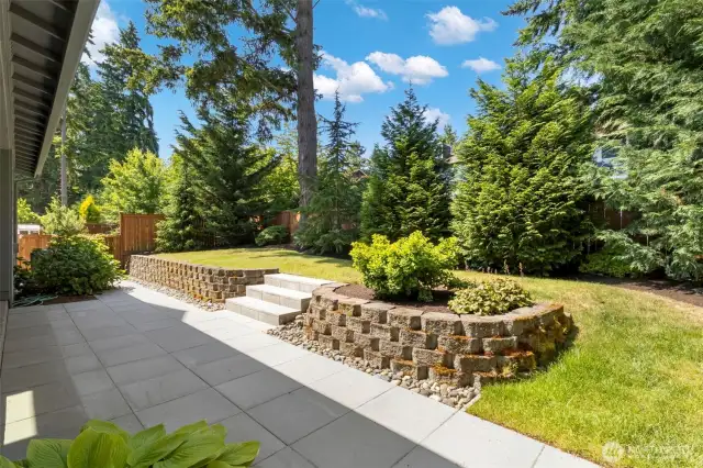 The backyard is a private, sun-dappled oasis bordered by mature evergreens and thoughtfully landscaped with tiered garden beds and stone retaining walls. With a spacious patio and lush lawn, it’s perfect for relaxing, entertaining, or simply enjoying the serenity of nature.