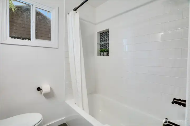 Crisp, modern tub/shower combo with fresh white subway tile surround, stylish black-and-white geometric accent niche, matte-black fixtures, and a large window for natural light. Clean, bright, and fully updated – the perfect spa-inspired retreat.