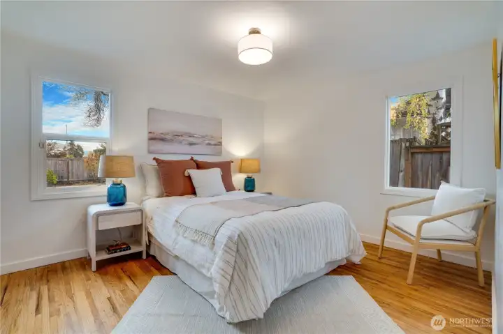 Peaceful and spacious primary bedroom featuring newly refinished hardwood floors, two sunny windows with backyard views, fresh designer lighting, and plenty of room for a king-size bed plus sitting area. Calm, bright, and completely updated – your perfect retreat at the end of the day.