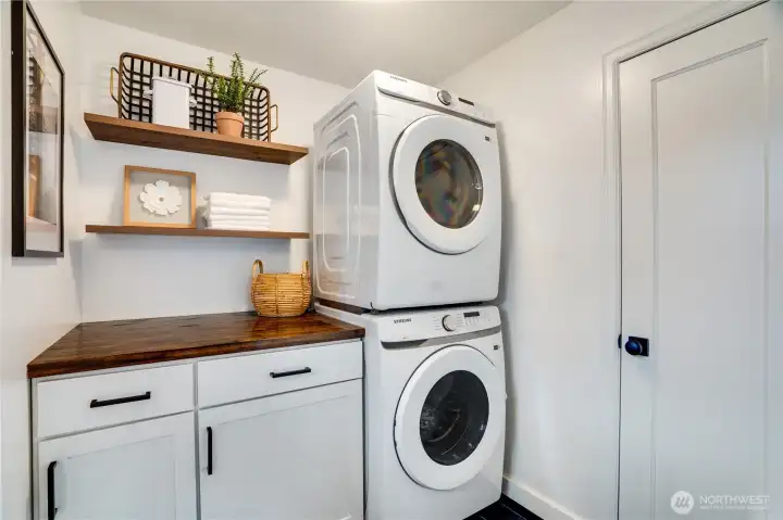Convenient dedicated laundry room with brand-new Samsung front-load washer and dryer (stacked), custom folding counter with butcher-block top, shaker cabinets for storage, open shelving, and stylish finishing touches. Clean, bright, and perfectly organized.