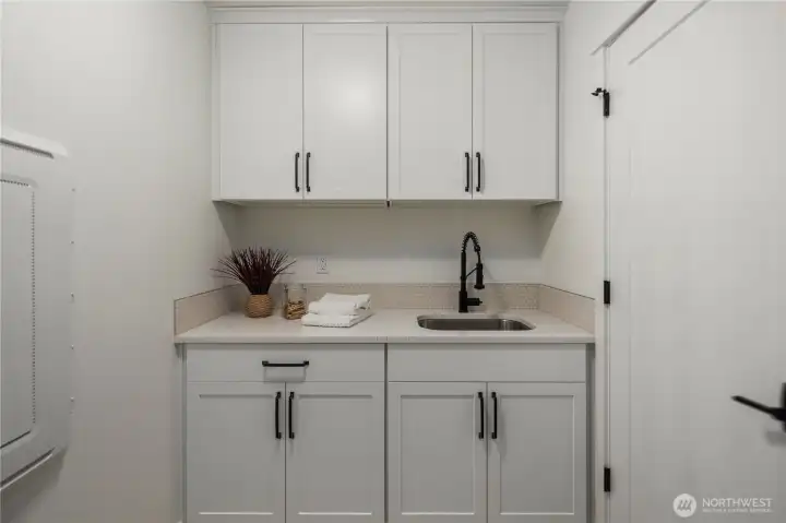 Laundry Room: Bright and functional laundry space with upper and lower cabinetry, quartz counters, and a deep sink for easy cleanup. The washer and dryer hookup is ready for your appliances, and extra storage keeps everything organized. Staged photos are of the model home of the same floorplan within the Foxmoore community and are for visualization purposes only. Colors, finishes, and layout can and will vary.