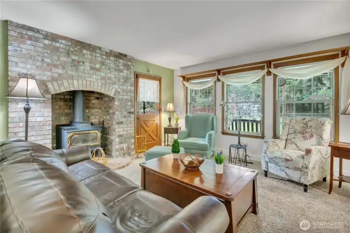 Bright living area with wood-trimmed windows and a substantial brick alcove for the woodstove, perfect for warmth and comfort.