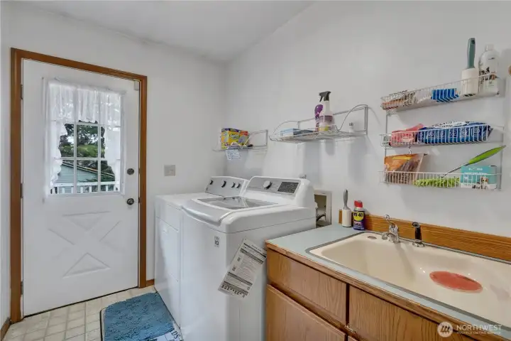 Well-appointed utility room featuring a sink, ample lower cabinets, and a door providing direct access to the back deck.