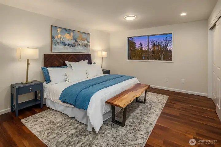 Your primary retreat awaits. This generous bedroom offers warm wood tones, a large picture window with sunset views, and ample space for a king-sized suite.