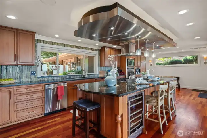Chef's kitchen centered around an oversized granite island, custom stainless hood, and built-in wine fridge — finished with rich cherry cabinetry and glass tile backsplash Chef's kitchen centered around an oversized granite island, custom stainless hood, and built-in wine fridge — finished with rich cherry cabinetry and glass tile backsplash