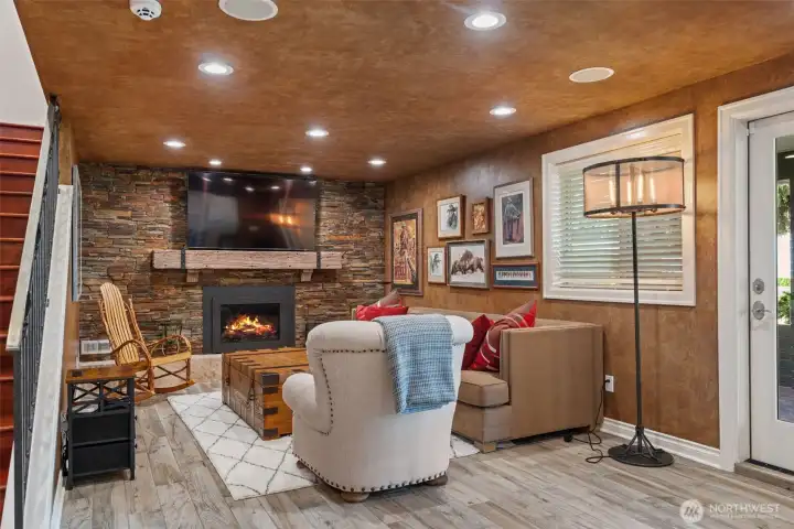 Lower-level family room with a cozy stacked stone fireplace, rustic wood mantel, and rich, character-filled finishes — a warm gathering space for movie nights or relaxing by the fire Lower-level family room with a cozy stacked stone fireplace, rustic wood mantel, and rich, character-filled finishes — a warm gathering space for movie nights or relaxing by the fire