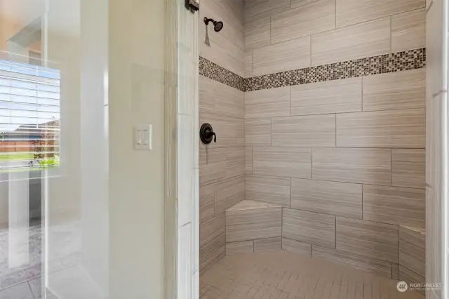 Custom tiled walk-in shower with inlay, glass door, and two shower heads.