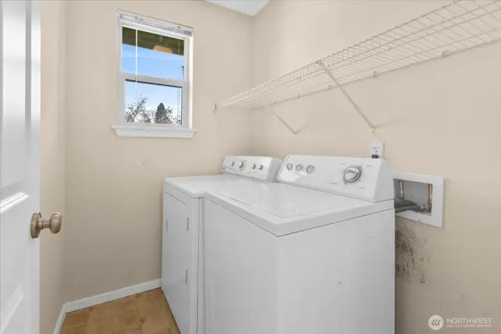 Laundry room with washer and dryer, wall-mounted wire shelf, and window providing natural light.