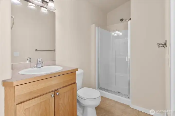 Ensuite bathroom with single-sink vanity, wall mirror, toilet, and glass-enclosed shower.