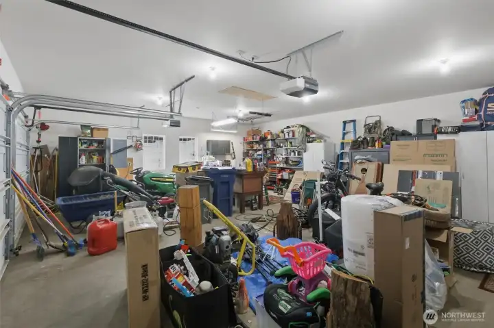 Oversized garage with shelving, refrigerator, and a John Deere Riding Mower for your enjoyment.