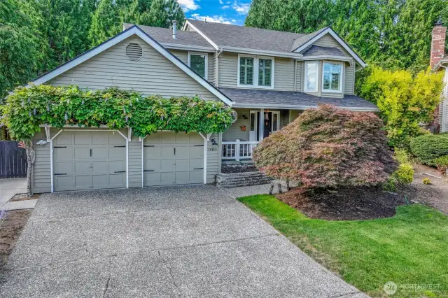 A wide driveway and two-car garage provide ample parking and convenience. The elevated front entry features terraced steps framed by lush greenery, setting a welcoming tone from the moment you arrive.