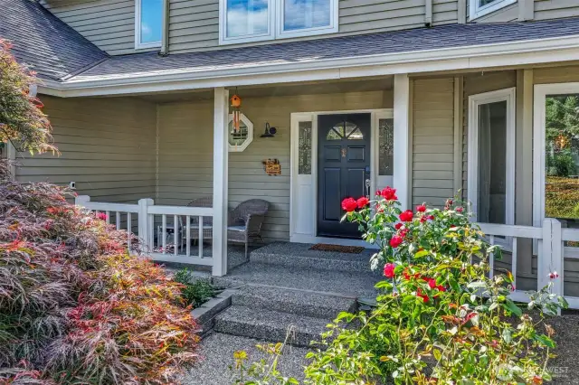 The covered front porch offers a peaceful spot to relax while enjoying the tranquil, tree-lined surroundings. The front entry is enhanced by decorative glass accents and a modern black door that adds contrast and character.