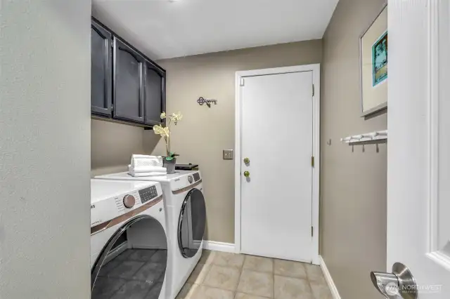 A dedicated laundry room off the garage features brand-new washer and dryer, upper cabinetry for convenient storage, and durable vinyl flooring—offering a clean, organized, and efficient space for handling household tasks.
