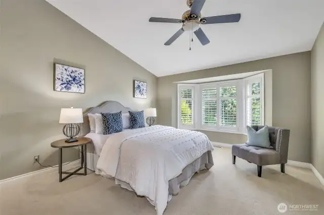 Upstairs, the spacious primary bedroom features vaulted ceilings, a ceiling fan, and a sunny bay window with plantation shutters—creating a peaceful retreat overlooking the treetops and yard.