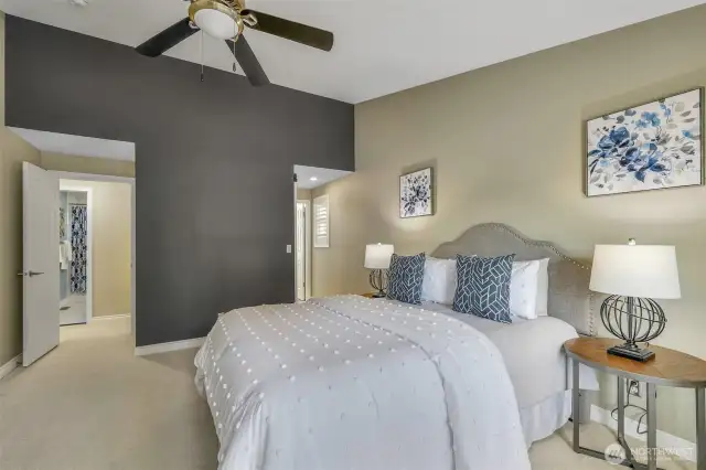 The vaulted ceiling and neutral palette continue in the primary suite, offering a spacious layout and a versatile sitting or reading area, enhanced by soft natural light.